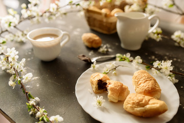 Croissants and coffee with milk on a black background with flowering branches of cherry

