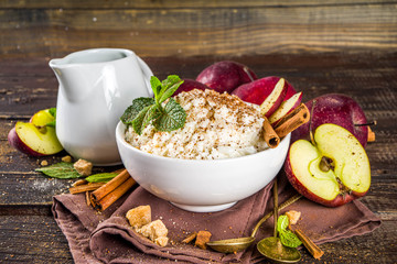 Hot autumn breakfast or lunch porridge or pudding with apple and spices. Rice porridge with cinnamon and red apples, on a wooden rustic background.