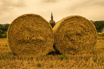 Beautiful polish field view with large round bales of straw (hay) and church in the background. Countryside landscape of Niemcza, Poland.