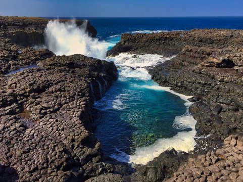 Buracona - The Blue Eye of Cabo Verde - blue lagoon inside a black rock with ocean splash in the back 