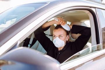 Woman with protective mask at her face and sitting in the car and brush her hair. Quarantine concept