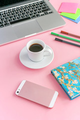 a coffee mug stands on a notebook, next to it lies a phone, pens and a laptop