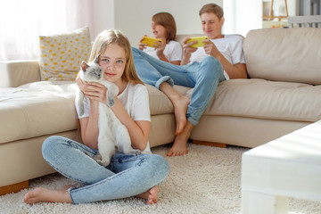 Children at home each play their own game. Brother and sister are playing at home. The child plays on the phone. A child is playing with a cat.