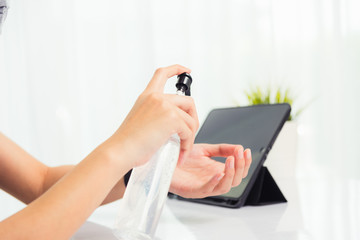 Asian Business young woman working from home office he quarantines disease coronavirus or COVID-19 wearing a protective mask and cleaning hands with sanitizer gel on front tablet computer