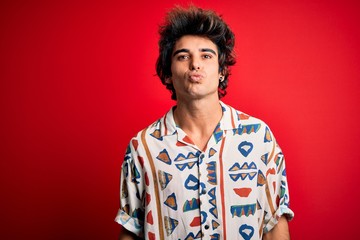 Young handsome man on vacation wearing summer shirt over isolated red background looking at the camera blowing a kiss on air being lovely and sexy. Love expression.