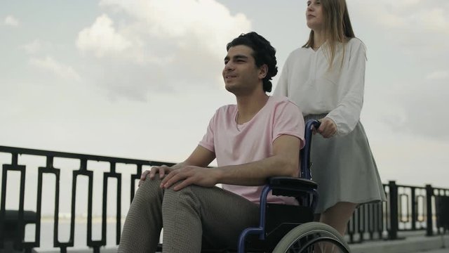 woman carry disabled man in the wheelchair - they are talking and laughing