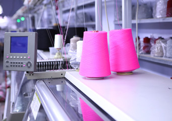 Pink spools of thread on the background of the sewing workshop. Clothing industry. Machine for the...