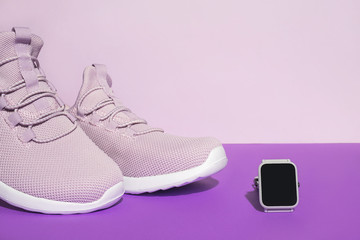 Fototapeta na wymiar New purple sneakers and smart watch on colorful background with copy space. Healthy lifestyle concept.