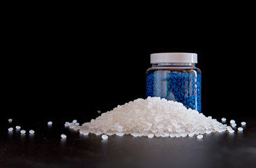 White plastic and blue plastic beads in plastic bottles on black background, Polymers bead or polymer resin, polymer pallet, Product from petrochemical plants.