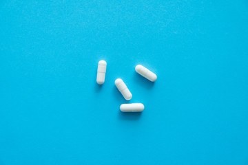 White pills on blue background. Medicine, medication, painkillers, tablet, medicaments, drugs, antibiotic, vitamin, treatment. Pharmacy theme. Top view on the pills scattered on the blue surface.