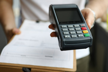 Close-up of delivery service and man holding cashier machine for payment. Nfc technology counter. Person with clipboard for sign. Client make transaction pay bill on terminal