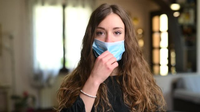 Giovane bella ragazza sorride in camera a casa togliendosi la mascherina 