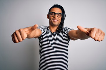 Fototapeta premium Young handsome african american man with dreadlocks wearing striped t-shirt and glasses approving doing positive gesture with hand, thumbs up smiling and happy for success. Winner gesture.