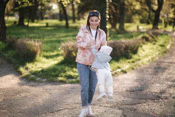Beautiful mom with adorable daughter walk in the park. Happy family spend time in Mother's Day. Cute little girl with mother spin around. Stylish family