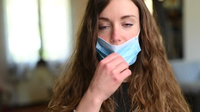 Giovane bella ragazza sorride in camera a casa togliendosi la mascherina 
