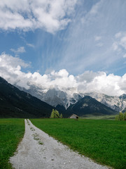View on Tyrol mountains with green meadow and a gravelly path leading towards the mountains. With partly cloudy sky.