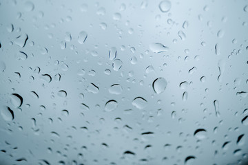 Drops of water running down the windshield of a car. Photo taken from a low angle, so the dark sky can be seen vaguely through the raindrops.
