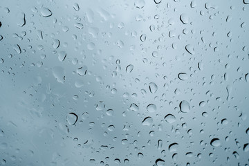 Drops of water running down the windshield of a car. Photo taken from a low angle, so the dark sky can be seen vaguely through the raindrops.