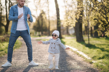 Adorable little gilr spend time with her father. Dad and daughter walk in the park. Stylish family. Happy little girl in sunglasses. Dad and daughter dance in the park