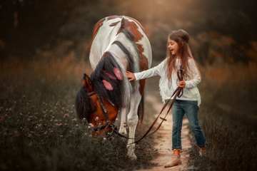 Little girl in indian style with pinto pony in a summer field in sunny evening