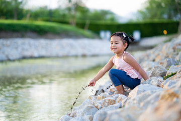 Adorable girl sitting at pond in summer.