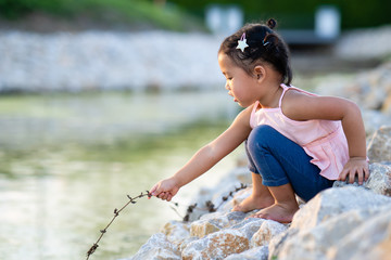 Adorable girl sitting at pond in summer.