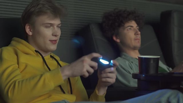 Young gamers in a movie theater, two friends playing video games on a game console, playing games on a big screen.