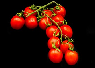 red cherry tomatoes with a green stem lie on a black background top view, isolated