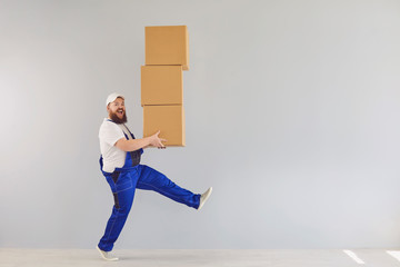 Funny fat bearded delivery courier loader man in a blue uniform with a cardboard box on a gray...