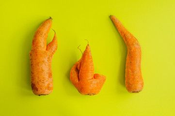 Ugly food. Deformed organic carrots on a green background. Concept of food waste. Minimalism, pop art style. Flat lay

