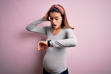 Young beautiful teenager girl pregnant expecting baby over isolated pink background Looking at the...