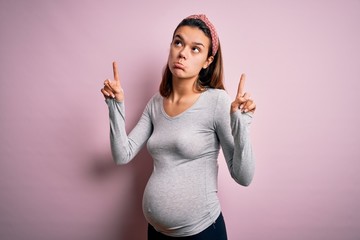 Young beautiful teenager girl pregnant expecting baby over isolated pink background Pointing up...
