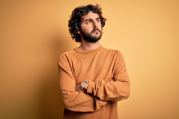 Obraz premium Young handsome man with beard wearing casual sweater standing over yellow background looking to the side with arms crossed convinced and confident