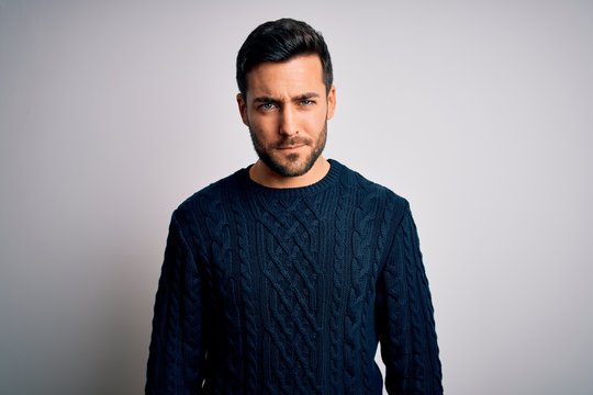 Young handsome man with beard wearing casual sweater standing over white background skeptic and nervous, frowning upset because of problem. Negative person.