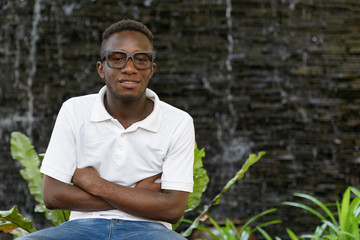 Naklejka na ściany i meble Happy young African man with eyeglasses smiling with arms crossed outdoors
