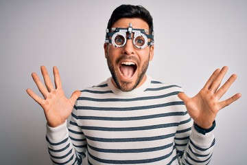 Naklejka premium Young handsome man with beard wearing optometry glasses over isolated white background celebrating crazy and amazed for success with arms raised and open eyes screaming excited. Winner concept