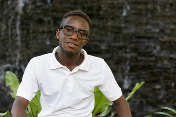 Naklejka na ściany i meble Portrait of happy young African man with eyeglasses smiling outdoors
