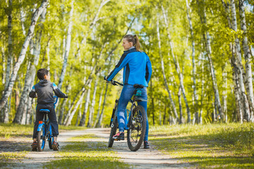 Funny boy cyclistrides a bike with mom in the sunny forest on a bike. Adventure travel.