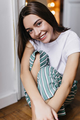 Pretty smiling girl posing in casual striped pants. Wonderful dark-haired female model sitting on the floor and laughing.