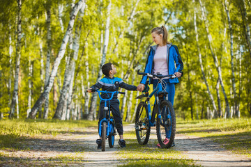 Naklejka premium Funny boy cyclistrides a bike with mom in the sunny forest on a bike. Adventure travel.