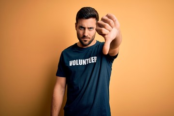 Young handsome man with beard volunteering wearing t-shirt with volunteer message with angry face,...