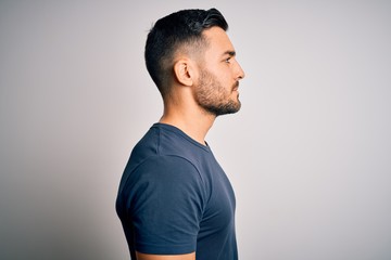 Young handsome man wearing casual t-shirt standing over isolated white background looking to side, relax profile pose with natural face with confident smile.