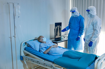 Female elder patient is listening to African and European doctors in full personal protective equipment suit for positive diagnostic result. Infected lady gets information from two medical doctors