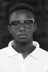 Face of young African nerd man wearing eyeglasses outdoors in black and white