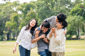 Asian happy family have playing time together in park in nice weather. Boy kid sit on father shoulder and hold hands laughing with mother and grandmother. Family lifestyle relax and leisure concept.