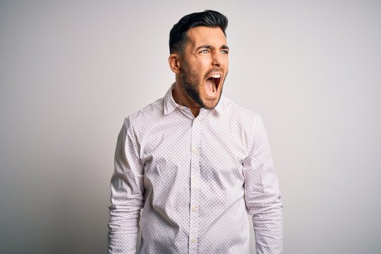 Young handsome man wearing elegant shirt standing over isolated white background angry and mad screaming frustrated and furious, shouting with anger. Rage and aggressive concept.