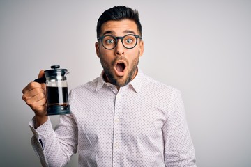 Young handsome man making coffee using french press coffeemaker over isolated background scared in shock with a surprise face, afraid and excited with fear expression