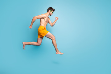 Fototapeta na wymiar Full length body size profile side view of nice attractive cheerful purposeful guy in swimming shorts jumping running fast isolated on bright vivid shine vibrant green blue turquoise color background