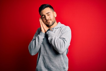 Young handsome sportsman wearing sweatshirt standing over isolated red background sleeping tired dreaming and posing with hands together while smiling with closed eyes.