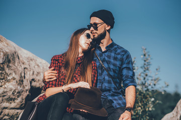 Fototapeta premium A hipster traveler couple sitting together on the rocks at the mountains. Toned photo